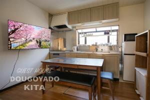 a kitchen with a table and a tv on the wall at GUEST HOUSE DOUGOYADO KITA in Matsuyama