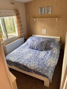 a bedroom with a bed with a blue comforter and a window at 4-Bedroom Cosalt Parkhome in Uddingston, Glasgow in Uddingston