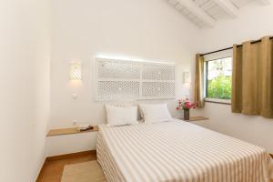a white bedroom with a bed and a window at Pedras D'el Rei in Tavira