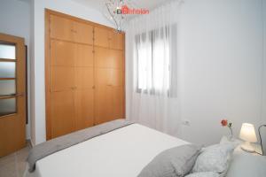 Un dormitorio con una cama blanca y un armario de madera. en Banda Playa - Arizón, en Sanlúcar de Barrameda