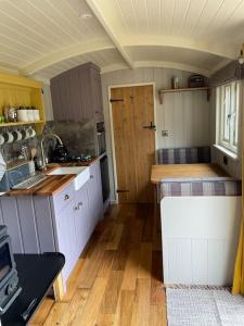 a kitchen with white cabinets and a wooden floor at The Old Post Office - Luxurious Shepherds Hut 'Far From the Madding Crowd' based in rural Dorset. in Todber
