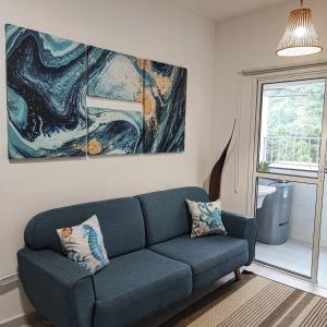 un sofá azul en una sala de estar con una pintura en Apartamento novo e completo, próximo à praias e comércio en Ubatuba