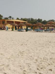 Villa Nesrine في Hammamet Sud: شاطئ رملي عليه مظلات وكراسي