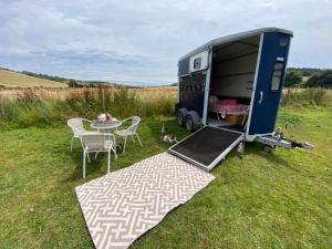 a rv parked in a field with a table and chairs at Glamping with a twist in Charlton
