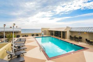 a pool with chairs and tables and the ocean in the background at Beach Quarters Resort in Virginia Beach