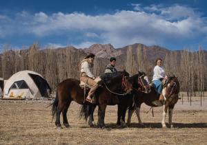 three people riding horses in a field with a tent at Cinco Cumbres in Uspallata