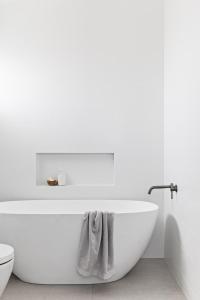 een witte badkamer met een bad en een toilet bij Cape Beach House in Byron Bay