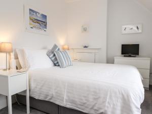 a white bedroom with a white bed and a tv at Whinstone Bamburgh in Bamburgh