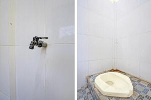 een badkamer met een toilet in een witte betegelde muur bij SPOT ON 92799 Tanjung Indah Homestay Syariah in Banyuwangi