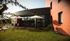 Un patio con mesas y sombrillas frente a un edificio. en Hotel Eurocentre 2* Toulouse Nord, en Castelnau-dʼEstrétefonds