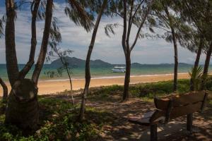 Un banco junto a una playa con un barco en el agua. en Pina Colada on the Beach - Beachfront - 2 Bedroom, en Mission Beach