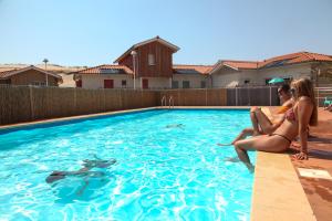 two women sitting on the edge of a swimming pool at Residence Plage Oceane in Biscarrosse-Plage