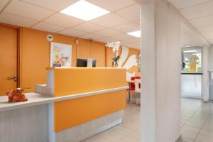 una sala de espera con paredes de color naranja y una recepción. en Premiere Classe La Ville Du Bois, en La Ville-du-Bois