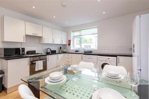 cocina con mesa de cristal y armarios blancos en Gertrude House - Spacious 3BR Bungalow in Nottingham, en Nottingham