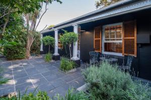 ein schwarzes Haus mit einer Terrasse mit Stühlen und Bäumen in der Unterkunft Snug Haven Cottage in Kapstadt