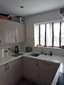 cocina con armarios blancos, fregadero y ventana en Cosy room with 3 bed spaces in a friendly bungalow en Bletchley