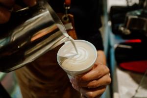 a person pouring milk into a cup of coffee at Herloom Hotel & Residence BSD Tangerang in Tangerang