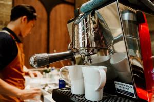 a man is making cups on a coffee machine at Herloom Hotel & Residence BSD Tangerang in Tangerang