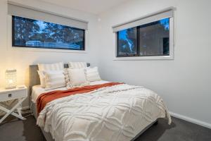 a white bedroom with a bed and two windows at Blyth Retreat, Bruny Island in Simpsons Bay