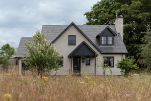 a white house with a black roof in a field at Balnagowan Cottage in Nethy Bridge