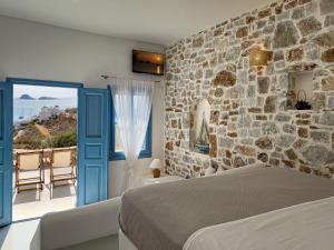 1 dormitorio con pared de piedra, cama y ventana en Sirocos, en Karavostasi