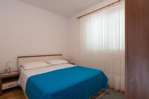 a white bedroom with a blue bed and a window at Apartments Mirko in Vinišće