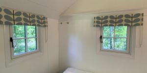 duas janelas com persianas romanas num quarto em Lingfield Shepherds Hut em Blindley Heath
