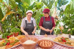 duas mulheres de avental em pé numa mesa com comida em Forte Village Resort - Pineta em Santa Margherita di Pula