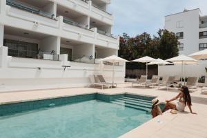 Dos mujeres están sentadas junto a una piscina. en Hoposa Pollensamar Apartamentos, en Puerto Pollensa