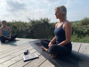 Dos mujeres sentadas en una terraza haciendo yoga en Basecamp Tiny House Eco Resort en IJmuiden