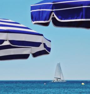 - un voilier dans l'océan avec un parasol bleu et blanc dans l'établissement Amerique Hotel Palavas - Piscine & Parking - Plage, à Palavas-les-Flots