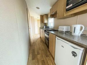 a small kitchen with wooden cabinets and a white dishwasher at Lovely 8 Berth Caravan With Decking At Eastgate Fantasy Island Park Ref 58004c in Skegness