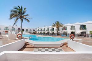 a swimming pool with palm trees and a building at Piso Relax - Carpe Mundi in Corralejo