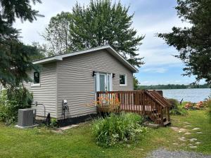 a small house with a wooden deck next to a lake at Modern, Sunset Waterfront Cottage with EV Charger in Yarker