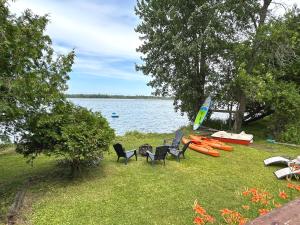a group of chairs and kayaks on the grass by the water at Modern, Sunset Waterfront Cottage with EV Charger in Yarker