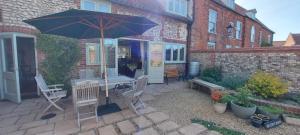 eine Terrasse mit einem Sonnenschirm, einem Tisch und Stühlen in der Unterkunft Beatrix Barn in Burnham Market