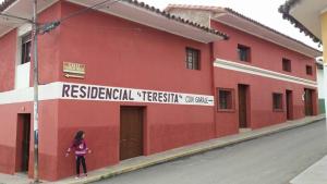 a girl standing in front of a red building at Residencial Teresita in Vallegrande