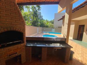 a brick fireplace with a swimming pool in a backyard at Linda casa Condomínio Costa do Sol - Bertioga in Bertioga