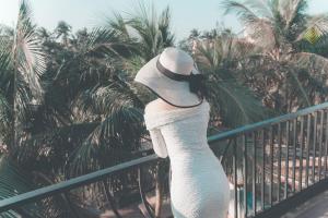 une femme en robe blanche et chapeau sur une clôture dans l'établissement G Boutique Resort Hoi An, à Hội An