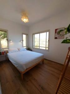 a bedroom with a bed with white sheets and windows at בקצה in Ma'ale Gamla