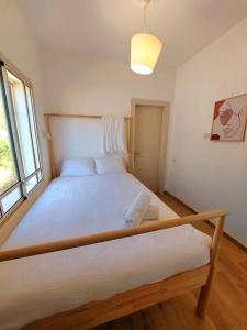 a bedroom with a large white bed with a window at בקצה in Ma'ale Gamla