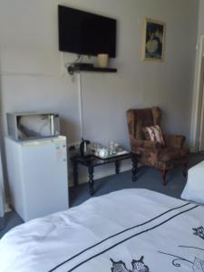 um quarto com uma televisão, uma cadeira e uma cama em Kwa-Dlamathe Guesthouse em Volksrust