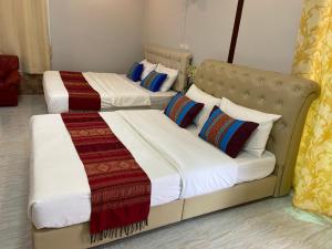 two beds in a hotel room with white sheets and colorful pillows at บุญจินดา รีสอร์ท in Ban Phayom