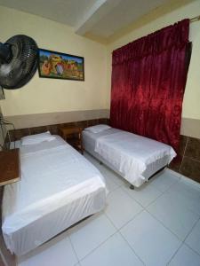 Habitación con 2 camas y ventilador en la pared. en Hostal Yahuarcaca, en Leticia