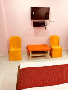 a room with two orange chairs and a tv at Hotel Tathastu in Rāmtek