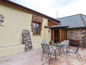 eine Terrasse mit einem Tisch, Stühlen und einem Sonnenschirm in der Unterkunft Quoit X Barn in Tiverton