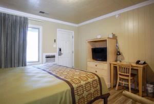 a bedroom with a bed and a desk and a television at Green Gables Motel & Suites in Burney