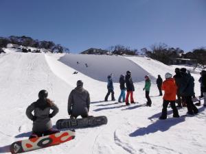 a group of people sitting on top of a snow covered slope at Sundeck Hotel in Perisher Valley