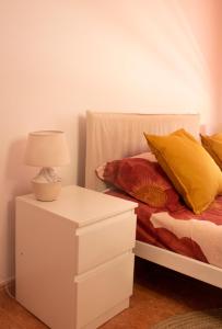 Cama blanca con almohadas amarillas y mesita de noche con lámpara en Apartamento Veronika en Arrecife