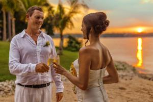 a man and a woman standing on the beach with a glass of champagne at The Oberoi Beach Resort, Lombok in Tanjung